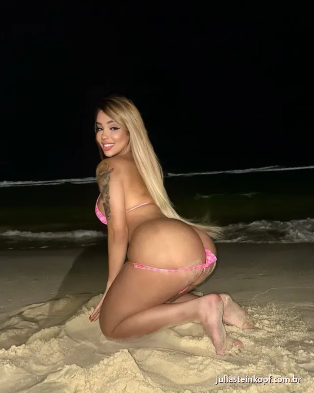 Júlia de biquíni rosa na areia da praia, à noite